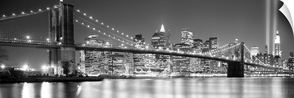 A panoramic landscape photo taken after 2001 of Manhattan and Brooklyn Bridge shining bright over the East River at night.