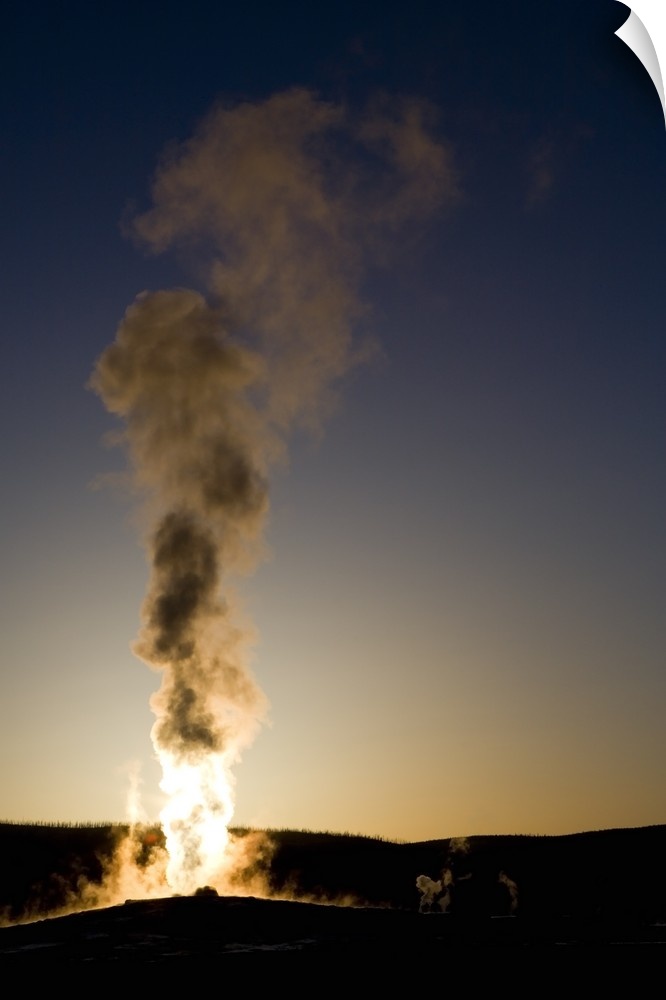 Portrait photograph on a big wall hanging of steam rising into the air as Old Faithful erupts as the sun sets.