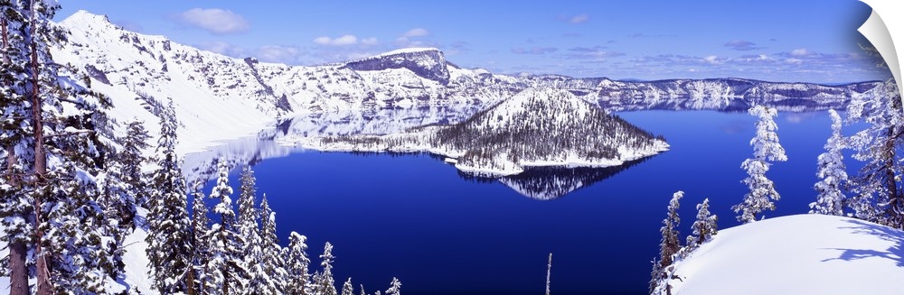 Wide angle shot taken of Crater lake looking out toward snow covered mountains and pine trees.