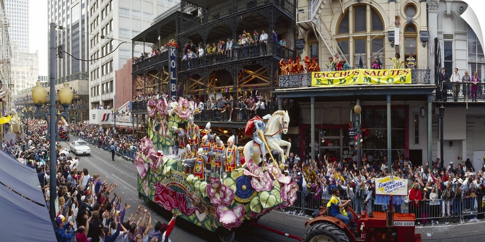 Large horizontal photograph of a tractor pulling a float through the crowded city streets of New Orleans, during the Mardi...