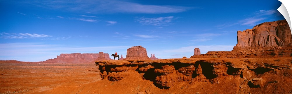 A man on a horse at the edge of a cliff overlooking the arid desert of Monument Valley on a clear day.