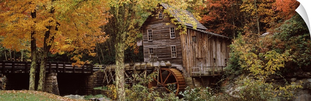 Wide angle view of an old mill surrounded by trees and foliage in the autumn. A small bridge is shown just to the left of ...