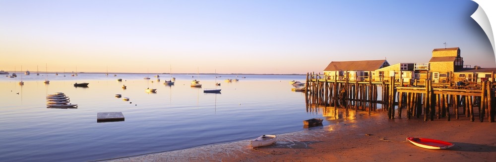 Picturesque panoramic photograph of a beach and small pier in Provinetown, Massachusettes. Small boats float in the ocean ...