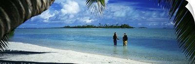 Rear view of two native teenage girls in lagoon, framed by palm tree, Aitutaki, Cook Islands