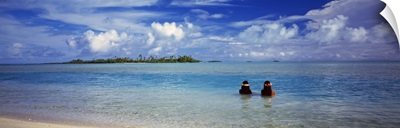 Rear view of two native teenage girls in lagoon water looking toward horizon, Aitutaki, Cook Islands