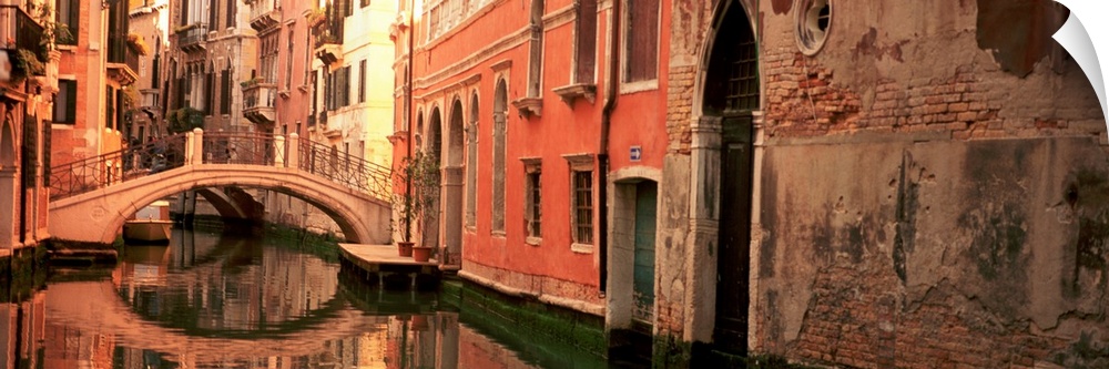 Panoramic photograph focuses on buildings and bridges following a canal in Venice, Italy.  Located on the surface of the w...