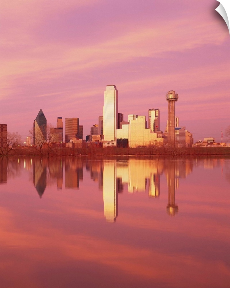 During sunset, the Dallas skyline is photographed from across a body of water that it reflects in.