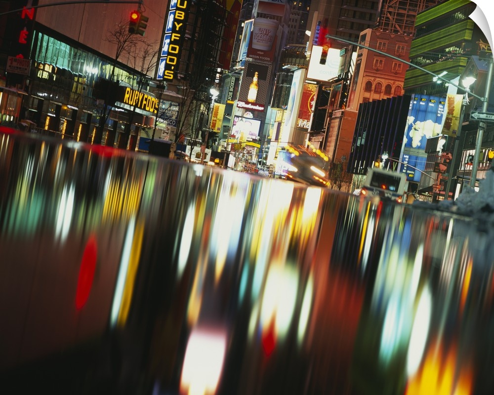 Evening photograph of the city, with neon lights and signs reflected in water, creating an abstract blurred effect.