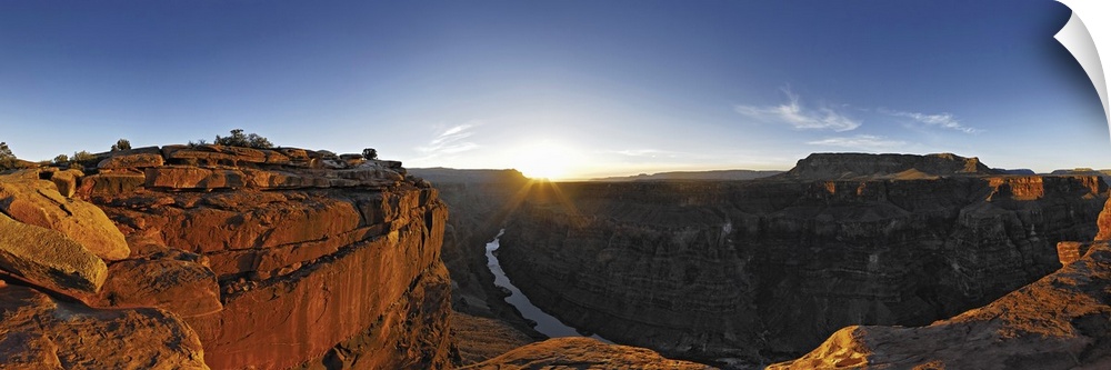A large panoramic photograph of the Grand Canyon with the river running through it and the sun setting on the horizon.