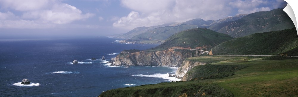 Large panoramic view of rock formations in the pacific ocean and immense mountains along the California coast.