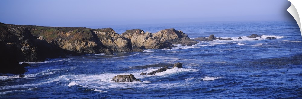 Wide angle photograph of the bright blue waters of Big Sur lapping around large rock formations near Garrapata State Beach...