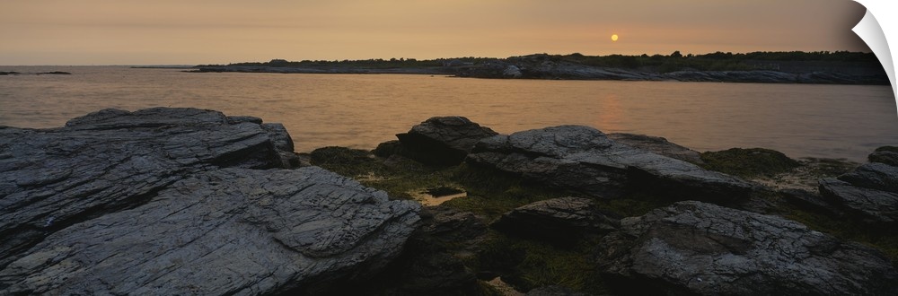 Wide angle photograph taken atop a rocky coast and looking out over a large body of water during sun down.