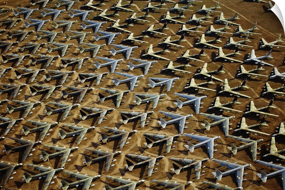 Field of retired airplanes arranged in a geometric pattern in the desert, shining in the sunlight and casting dark shadows.