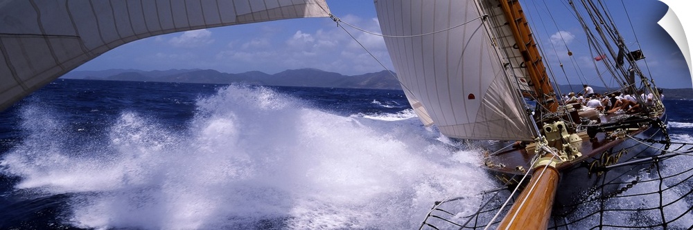 Panoramic photograph of wooden boat with sails making a hard turn and kicking up waves and sea spray in the ocean.