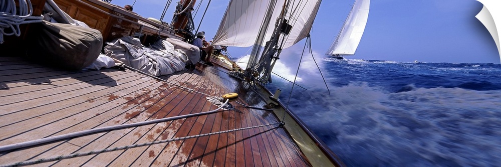 View from a boat of sails and cords stretched over the deck with ocean water splashing against the bow as it makes a sharp...