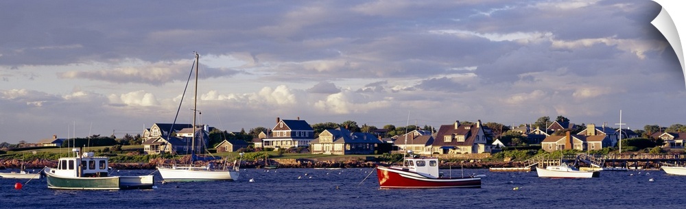 Large landscape photograph of many boast in Sakonnet Harbor, houses line the landscape, beneath a mostly cloudy sky in Rho...