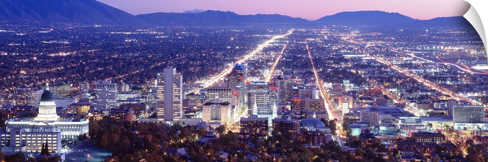Panoramic aerial photograph of city lit up at  night with mountain silhouettes in the distance.