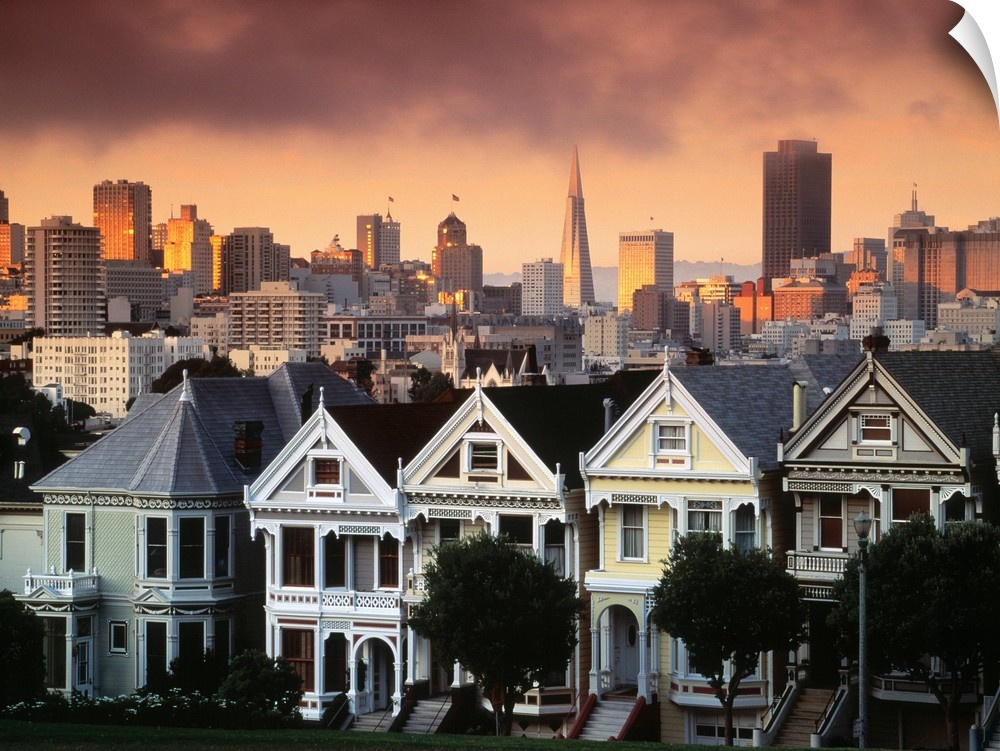 Photograph of pastel colored row houses with city skyline in the background at dusk.