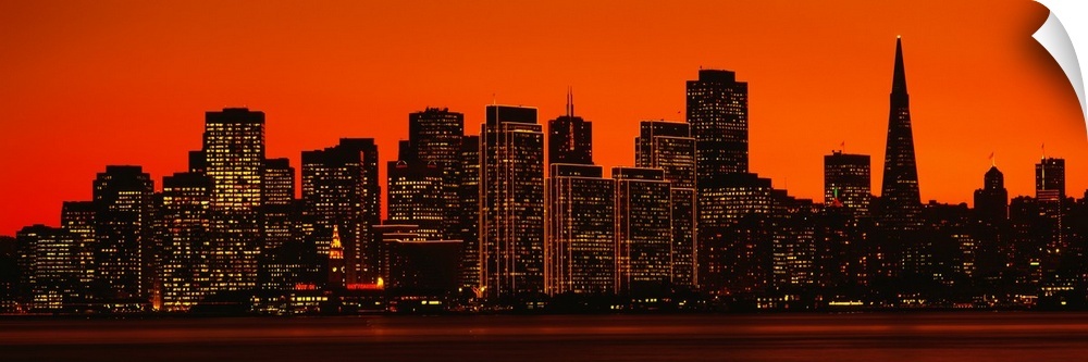 The skyline in San Francisco is pictured in wide angle view with a warm background silhouetting the buildings.