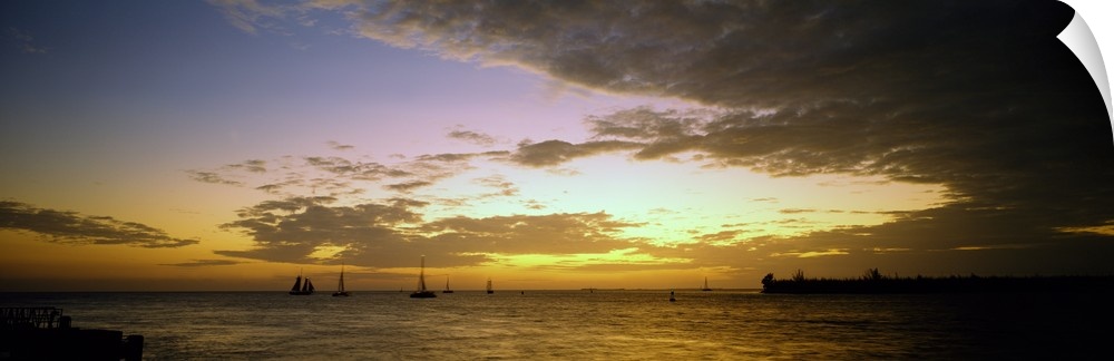 Panoramic photograph of ocean with sailboats in the distance under a cloudy sky at dusk.