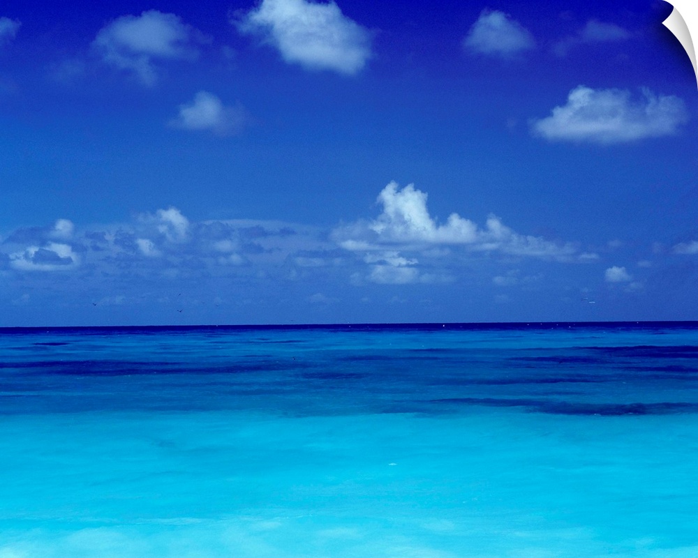 Big square photo art of a clear ocean with puffy clouds in a blue sky.