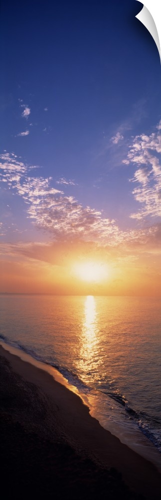 Vertical panorama of the sun rising on the horizon of the Atlantic ocean, as seen from a sandy beach in Western Europe.