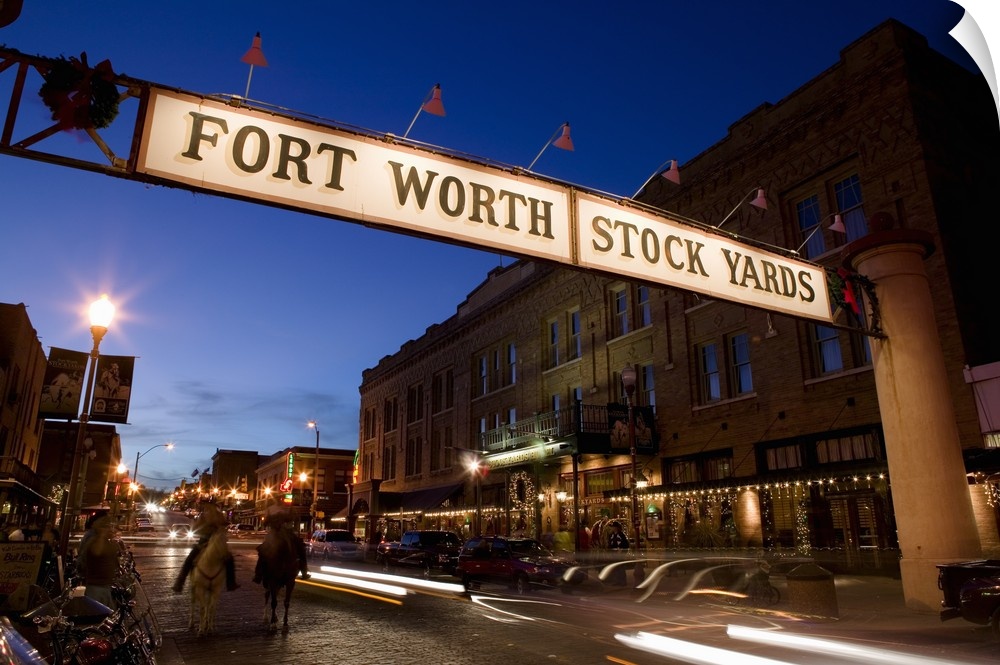 Landscape photograph of the Fort Worth Stock Yards sign over a road lined with buildings, at dusk in Texas.