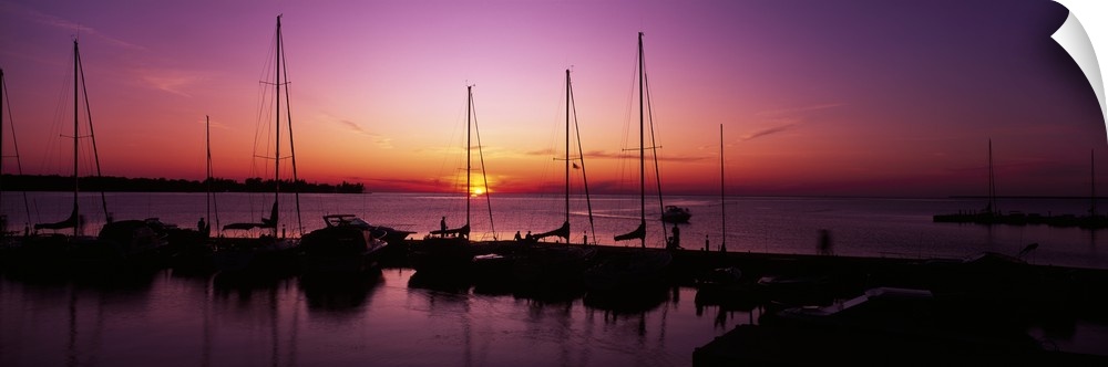 Several boats sit docked and silhouetted by the sunset that is about to dip below the horizon.