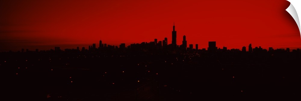 Panoramic photo of a dark silhouetted cityscape against a warm sky.