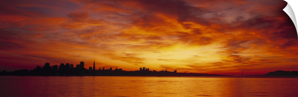 The San Francisco skyline is silhouetted by a beautiful sunset sky and viewed at a distance from across a body of water.