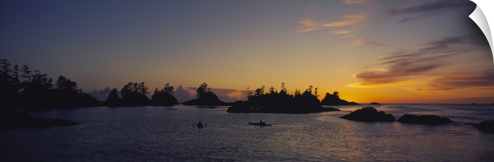 Tiny islands and boats on the water are silhouetted by the sunset that has gone below the horizon.