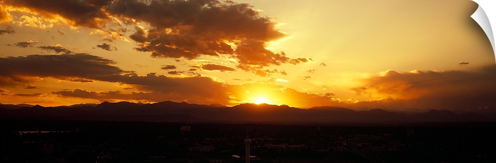 Land and mountainous terrain are silhouetted as the sun begins to rise from behind them.