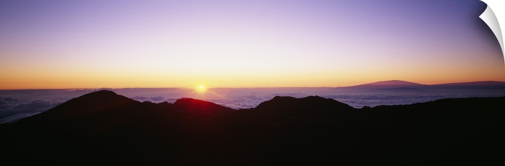 The sun begins to rise above the horizon and silhouettes a mountain range in the foreground of the picture.