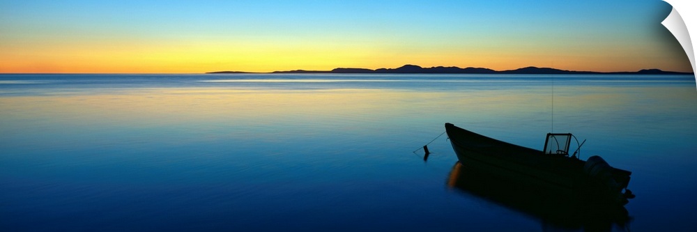 Lonely boat resting on the calm ocean as the fading sun emits a golden glow on the horizon.