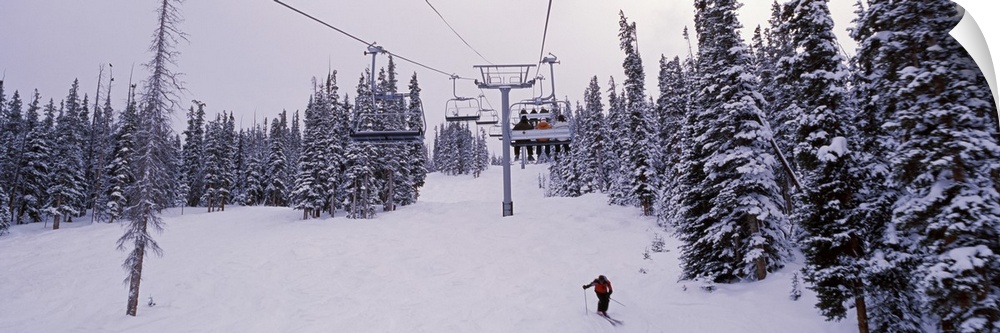 Panoramic photograph on a giant canvas of a ski lift surrounded by snow covered trees, one skier on the ground, at the Key...