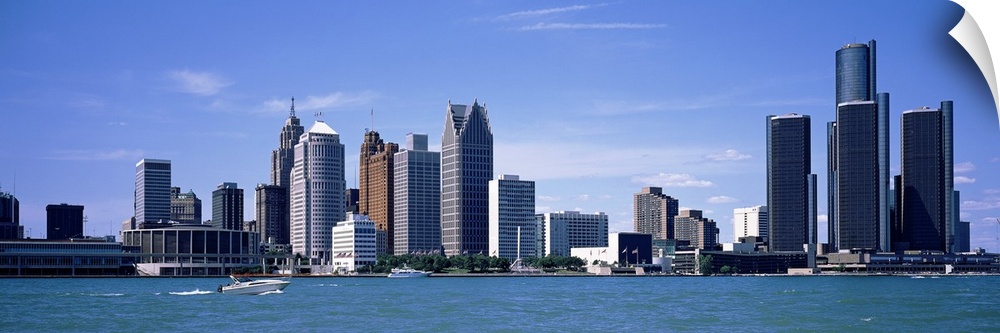 Panoramic photograph taken of the Detroit skyline during the day with a body of water shown in front of the buildings.