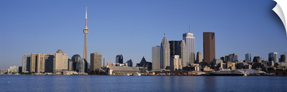 Panorama of a city skyline of tall modern buildings on the edge of a lake on a sunny day with a cloudless blue sky.