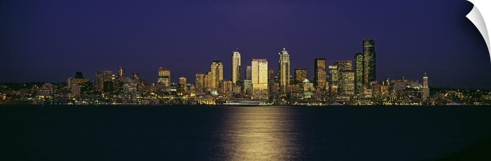 Wide angle, distant photograph of the Seattle skyline, lit at night, over Elliott Bay in Washington.