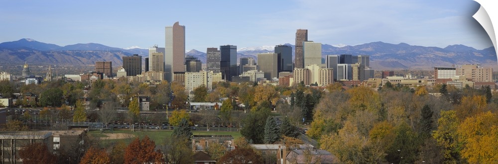An urban city skyline nestled in a Rocky Mountain valley with a baseball field and several trees along the edge.