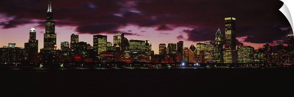 Wide angle photograph of the Chicago, Illinois skyline at night with brightly lit buildings against a deep purple sky.