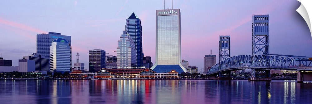 A panorama view of the city skyline in Jacksonville during dusk. The buildings lights reflect in the water that sits in fr...