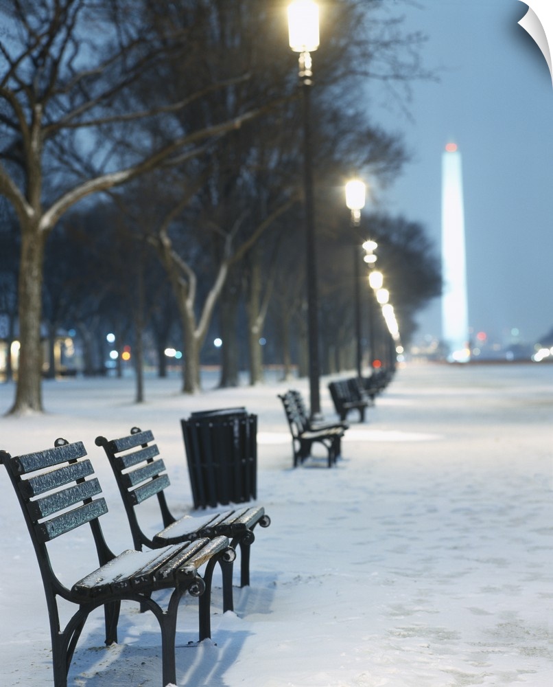 Snow covers the National Mall and rows of out of focus benches and street lights in this vertical landscape photograph.