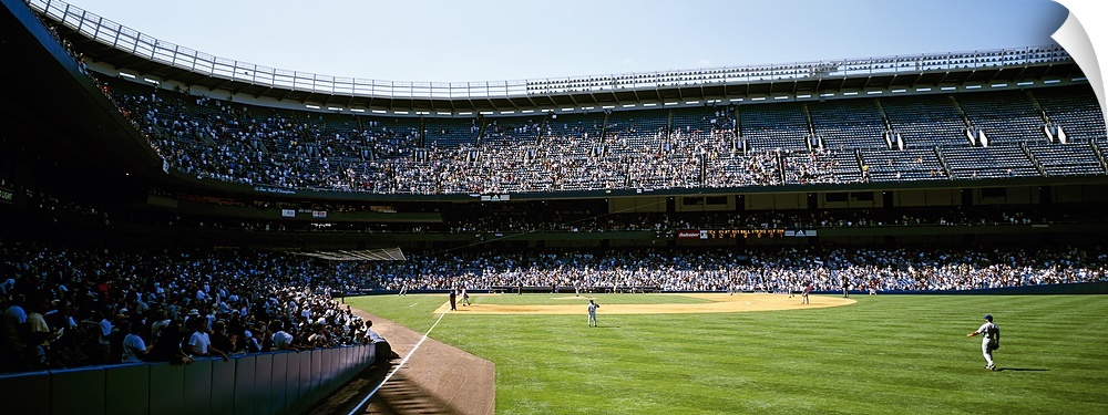 Wide angle photograph of Yankee Stadium with stands full of fans, during a baseball game in New York City.