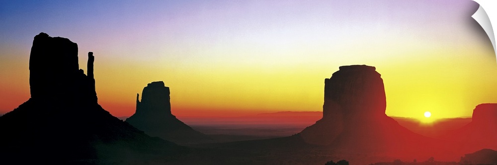 The sun begins to rise and silhouette Monument Valley in a wide angle view.