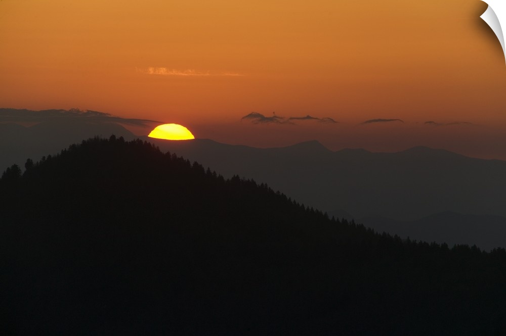 This landscape photograph captures the sun rising above the silhouettes of Appalachian mountains.