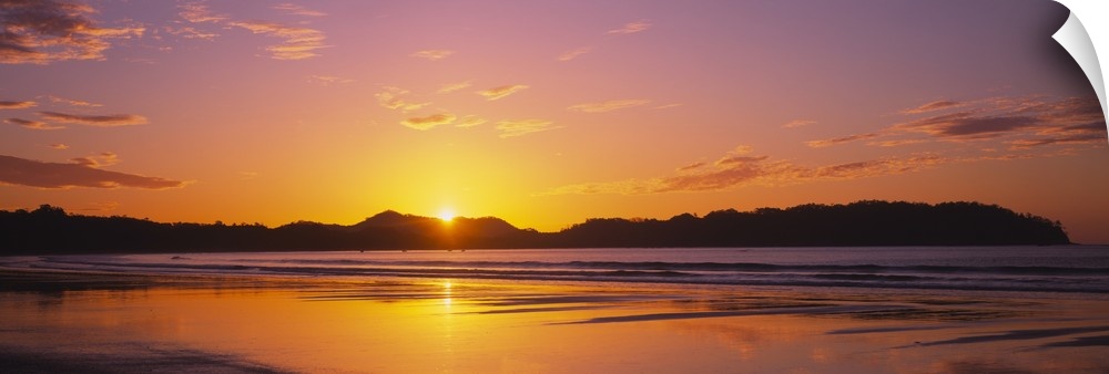 Long and horizontal image of the sun rising above a mountain near a beach in Costa Rica.