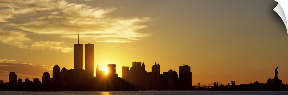 Panoramic photo of the sun rising right between two buildings in the silhouetted New York skyline, near the World Trade Ce...
