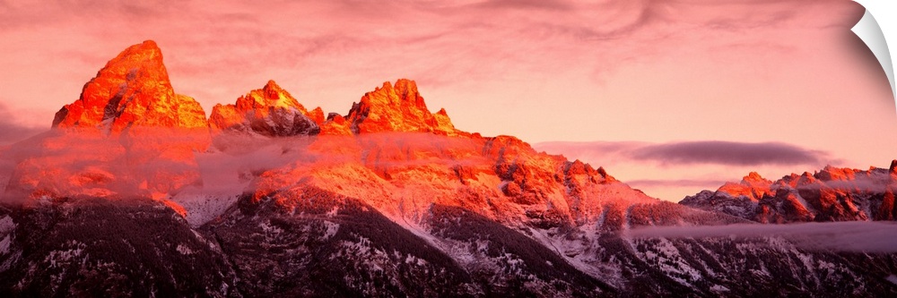 The sun rises on rugged mountains casting a warm hue of sunlight over the tops of them with darkness at the bottom.