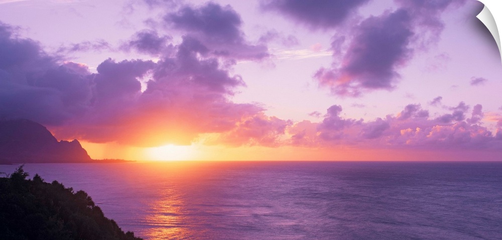 Sun setting on the ocean horizon creating a pastel-colored sky in the evening in Hawaii. Large lavender clouds float above...