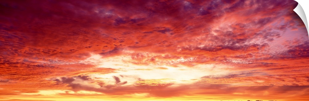 Panoramic photograph of a beautiful sunset sky with warm colored clouds gathered around the sun.